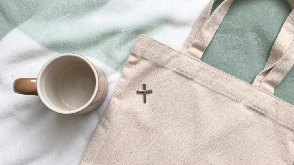 Ceramic mug, lapel pin, and tote on a soft surface with a hint of sage green